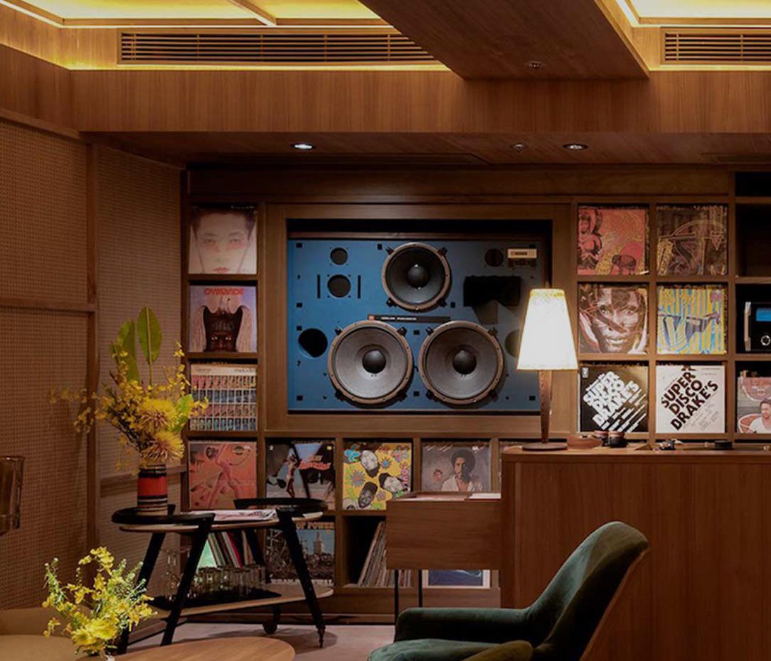Warm wood-panelled listening room with a large speaker system and vinyl records